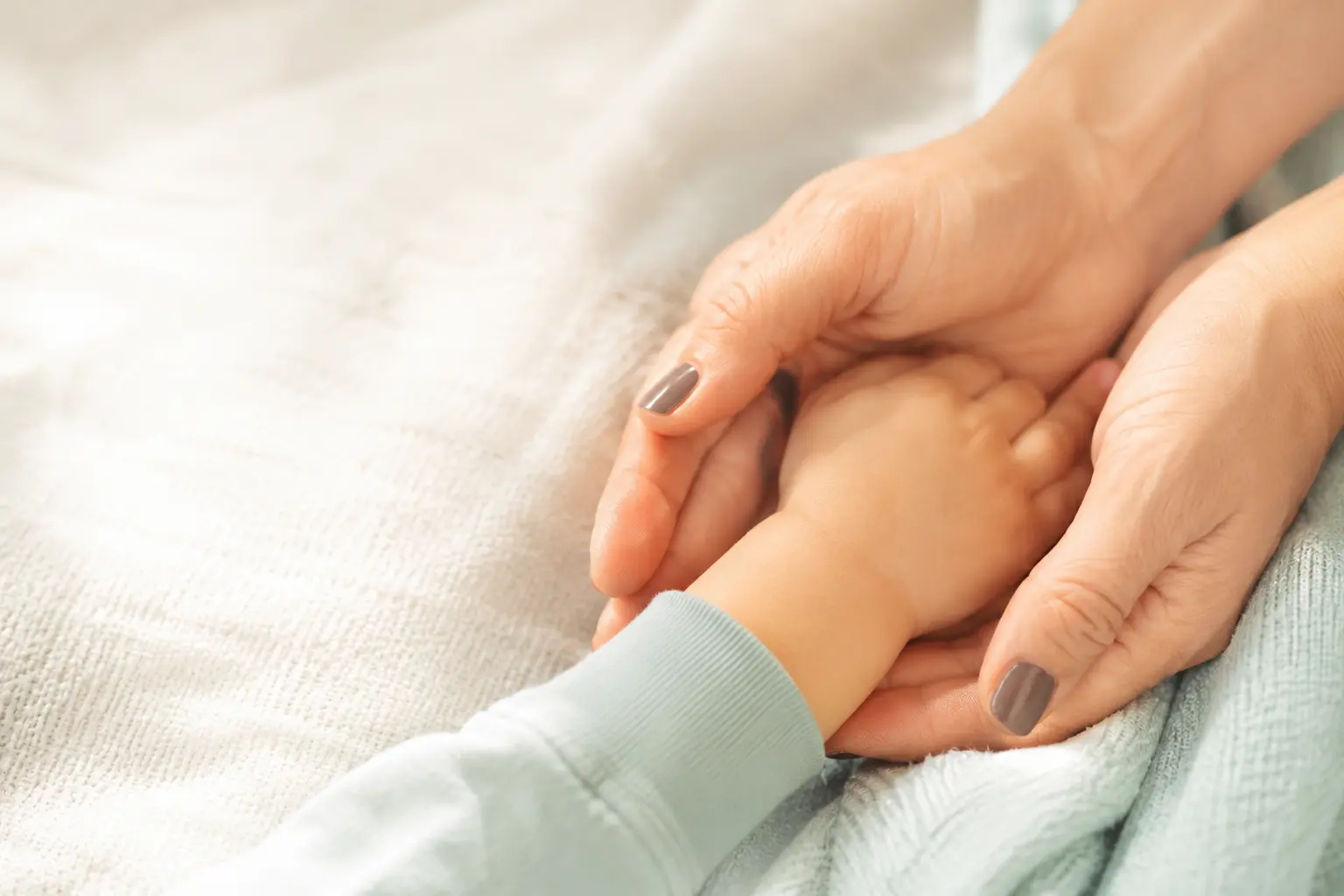 Elternhand und Kinderhand übereinander auf einer weichen Decke – die Familie hinter Wolkenhülle begleitet ihr Kind mit Neurodermitis.